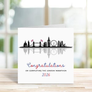 May include: A white greeting card featuring a black silhouette of the London skyline, including iconic landmarks like Big Ben and the London Eye. The card reads "Congratulations" in red and blue script, with "On completing the London Marathon 2026" below.