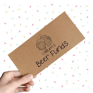 May include: A brown paper gift card with the text "Callum's Beer Funds" in a handwritten font. The card features a black illustration of two beer mugs. The background is white with colorful confetti.