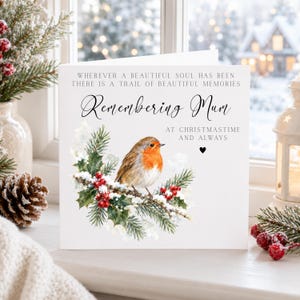 May include: A white greeting card featuring a watercolor illustration of a robin perched on a snowy pine branch with red berries. The text reads: WHEREVER A BEAUTIFUL SOUL HAS BEEN THERE IS A TRAIL OF BEAUTIFUL MEMORIES, Remembering Mum, AT CHRISTMASTIME AND ALWAYS.