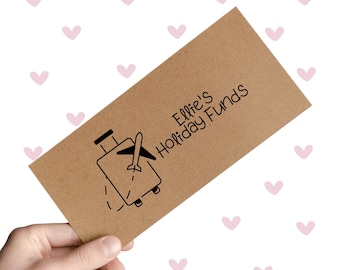 May include: A brown envelope with the text "Ellie's Holiday Funds" and a graphic of a suitcase with an airplane. The envelope is held against a white background with pink hearts.