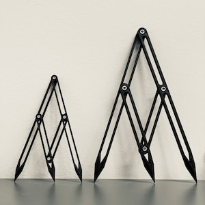 May include: Two black adjustable drafting tools, one larger than the other, are lying on a gray surface. The tools are made of metal and have a series of adjustable arms that can be used to create different shapes and angles.