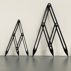 May include: Two black adjustable drafting tools, also known as a French curve, are shown on a gray surface. The larger tool is in the foreground and the smaller tool is in the background.