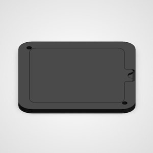May include: A rectangular, dark gray object with rounded corners. It features a recessed interior and a small notch on one side. Two small holes are visible on the surface, suggesting a possible mounting or attachment mechanism. The design is minimalist and modern.