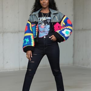 Puede incluir: Chaqueta vaquera con mangas de ganchillo coloridas, combinada con una camiseta negra con estampado y vaqueros negros. Las mangas presentan un diseño de patchwork con cuadrados azules, rojos, amarillos y verdes. El conjunto se completa con zapatos negros y beige.