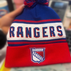 Pu&ograve; includere: Un berretto lavorato a maglia blu, rosso e bianco con un pompon. La parola "RANGERS" &egrave; al centro in lettere bianche. La parte inferiore del cappello &egrave; rossa con un logo della squadra che dice "Birmingham Rangers".