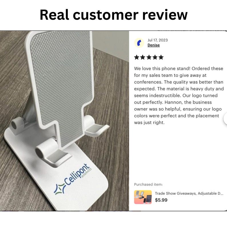 May include: White phone stand with a foldable design. The stand has a textured surface and a logo that says "Cellipont" in blue and white. The stand is on a wooden surface. The text "Trade Show Giveaways, Adjustable D... $5.99" is visible in the image.