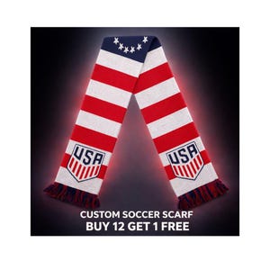 Può includere: Una sciarpa da calcio rossa, bianca e blu con la scritta "USA" su ciascuna estremità. La sciarpa ha un design a righe con una sezione blu con stelle bianche. La parte inferiore della sciarpa ha frange rosse e blu. Il testo in basso recita "CUSTOM SOCCER SCARF BUY 12 GET 1 FREE."