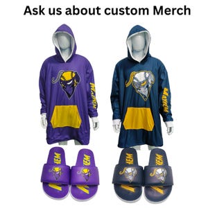 以下が含まれることがあります： フード付きスウェットシャツ2着とスライドサンダル2足。1着は紫で黄色のポケットとロゴ入り。もう1着はネイビーブルーで黄色のポケットとロゴ入り。スライドサンダルは紫とネイビーブルーで、ロゴが一致しています。「Ask us about custom Merch」と書かれています。
