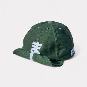 Può includere: Un cappellino da baseball verde scuro con visiera curva. Il cappellino presenta caratteri giapponesi bianchi sul lato e una piccola etichetta sul retro. Realizzato in tessuto strutturato.