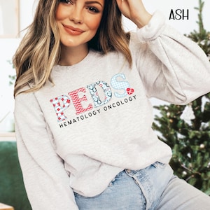 May include: A gray sweatshirt with the word "PEDS" in colorful patterned letters. The text "HEMATOLOGY ONCOLOGY" is written below the word "PEDS".