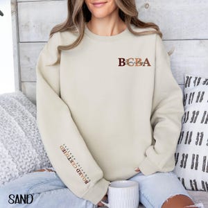 May include: A beige sweatshirt with the text "BCBA Emily" on the front and "Board Certified Behavior Analyst" on the sleeve.