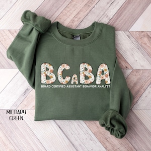 May include: A green sweatshirt with the text "BCBA Board Certified Assistant Behavior Analyst" printed on the front. The letters are decorated with a floral pattern.