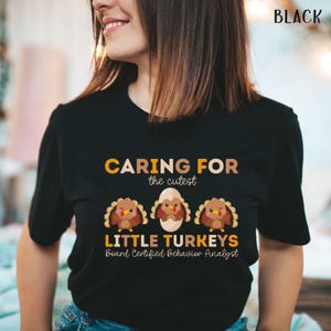 May include: Black t-shirt with the text "CARING FOR the cutest LITTLE TURKEYS Board Certified Behavior Analyst." The shirt features three cartoon turkeys, one hatching from an egg. The text is in yellow and brown.