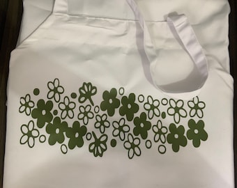 May include: White apron with a green floral design. The apron has a white neck strap and two white ties.