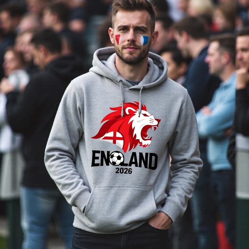 以下が含まれることがあります： 赤と白のライオンのデザインと、サッカーボールが付いた黒い文字で「ENGLAND」と書かれたグレーのフード付きスウェットシャツ。 年号「2026」が下に印刷されています。 画像の人物は顔にペイントを施しています。