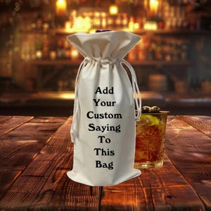 May include: White cotton wine bottle bag with black text that reads "Add Your Custom Saying To This Bag".