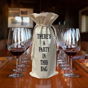May include: A white cotton wine bottle bag with black text that reads "There's a party in this bag".
