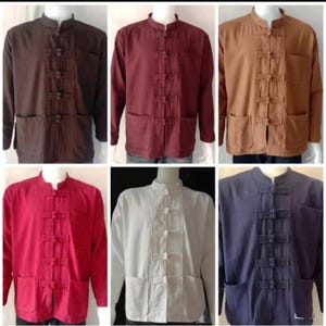 Può includere: Una collezione di camicie a maniche lunghe in vari colori: marrone, bordeaux, beige, rosso, bianco e blu navy. Ogni camicia presenta un colletto alla coreana, una chiusura con bottoni e due tasche frontali. Le camicie sono esposte su manichini.
