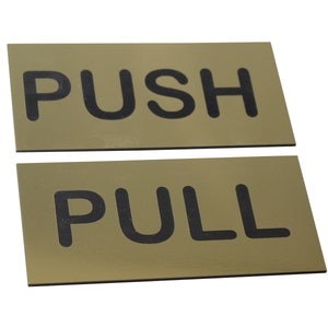 May include: Two rectangular door signs with the words "PUSH" and "PULL" in bold black letters. The signs have a gold-colored background and are set against a white background.