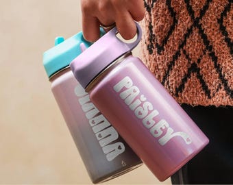 May include: Two stainless steel water bottles with carrying handles and lids. One bottle is light purple with the white text "Paisley" and small heart accents, while the other is a muted purple with the white text "Hannah" and heart accents.