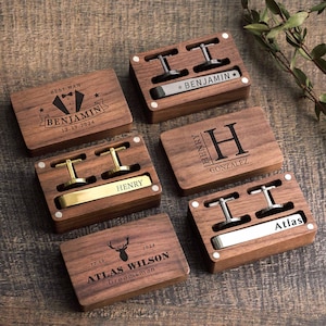 May include: A collection of personalized wooden cufflink boxes. Each box contains a pair of cufflinks and a tie clip. The boxes are engraved with names, initials, and dates. The cufflinks are silver and gold-toned.