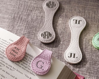 May include: Four magnetic bookmarks with textured surfaces. One pink bookmark reads EAT, PRAY, LOVE. One light purple bookmark features the letter G. One beige bookmark has a circular monogram KRM. One white bookmark displays the initials JL.