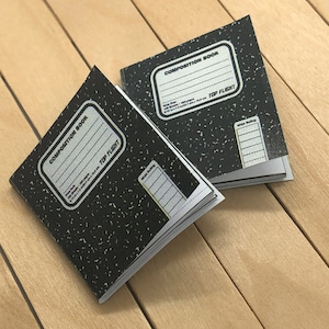 以下が含まれることがあります： 白い斑点のある黒い表紙のコンポジションノートが2冊。ノートには「Composition Book」と「Top Flight」のラベルが貼られています。