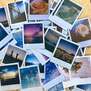 以下が含まれることがあります： 様々な色とサイズで、風景、花、人々を写したインスタント写真のコレクション。写真は木製の表面にランダムなパターンで配置されています。
