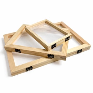 May include: Three rectangular wooden frames with a light natural finish, each featuring a clear glass front and small black metal hinges on the side. The frames are stacked at different angles, showcasing their simple construction and design.