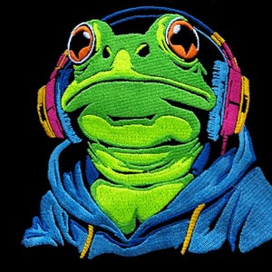 May include: Embroidered patch of a green frog wearing headphones. The frog has orange eyes and is wearing a blue hoodie. The headphones have pink, yellow, and blue accents. The patch is set against a black background.