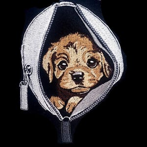 May include: Embroidered patch showing a brown puppy inside a zippered pouch. The puppy has large eyes and a black nose. The pouch is black with a silver zipper and trim, set against a black background.