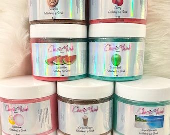 May include: A collection of nine clear plastic jars filled with colorful exfoliating lip scrubs, each featuring a white lid and a holographic label with the CharisMwah Beauty logo, scent name, and a 4 oz weight specification.