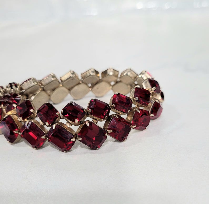 May include: A vintage bracelet with two rows of rectangular, deep red gemstones set in silver-toned metal. The faceted gemstones catch the light. The bracelet is a stretch style, designed to fit various wrist sizes.