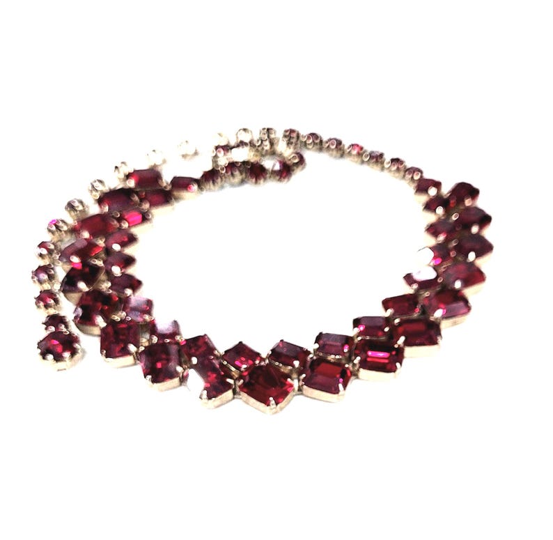May include: A vintage necklace with a series of rectangular and square-cut, deep red gemstones set in silver-toned metal. The necklace has a graduated design, with larger stones at the centre and smaller ones towards the clasp.
