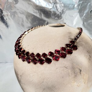 May include: A vintage necklace with a silver-tone metal chain and setting. The necklace features a series of rectangular, deep red gemstones. The gemstones are arranged in a geometric pattern, creating a bold and elegant statement piece.