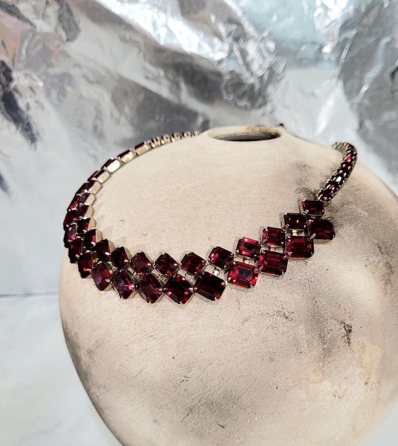 May include: A vintage necklace with a silver-tone metal chain and setting. The necklace features a series of rectangular, deep red gemstones. The gemstones are arranged in a geometric pattern, creating a bold and elegant statement piece.