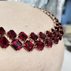 May include: A vintage necklace with two rows of rectangular, deep red gemstones set in gold-toned metal. The gemstones are closely set, creating a continuous band of colour. The necklace is displayed on a neutral-toned surface.