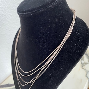 Puede incluir: Un collar de plata de múltiples cadenas con un diseño delicado. El collar se muestra en un maniquí de terciopelo negro.