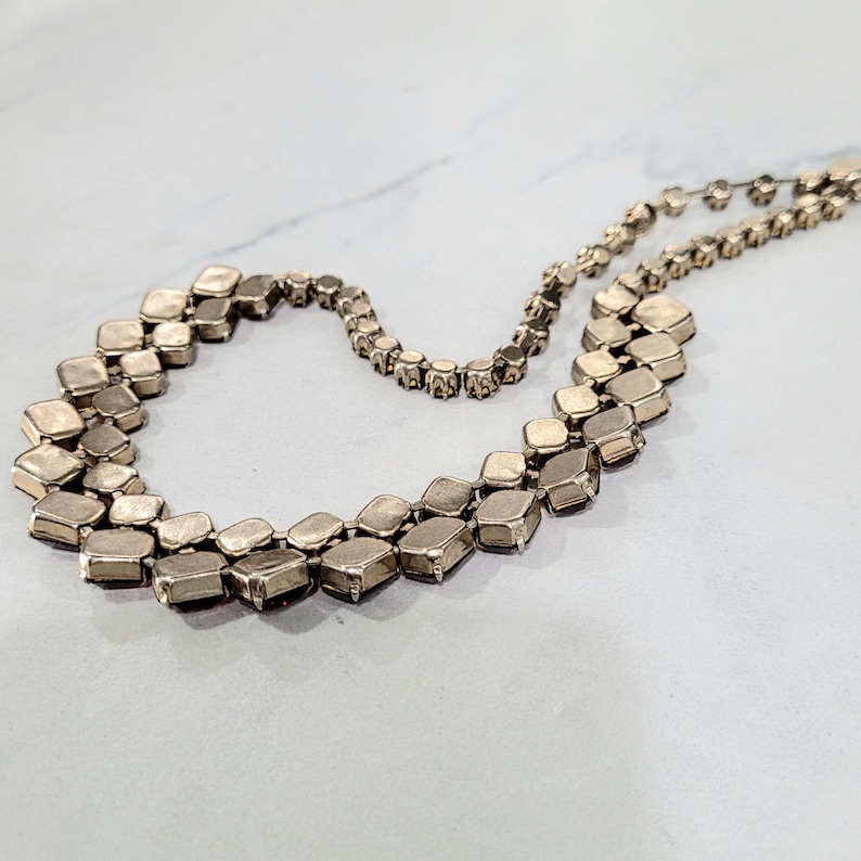 May include: A vintage necklace with a double strand design. The necklace features square-shaped, silver-toned stones. The stones are set closely together, creating a continuous, sparkling effect. The necklace is displayed on a white surface.