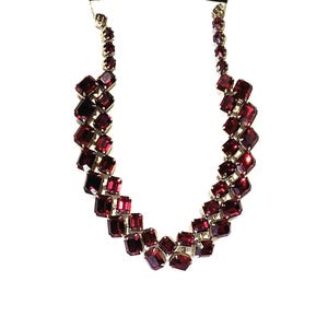 May include: A striking necklace with a series of rectangular, deep red gemstones set in silver-toned metal. The stones are arranged in a cascading pattern, creating a bold design. The necklace is displayed against a white background.