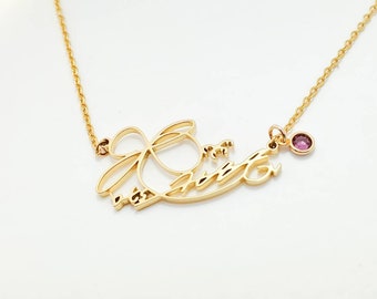 May include: A gold-toned necklace featuring a cursive script name pendant that reads "Jess" with an integrated loop design. The necklace includes a delicate gold chain and a single small, round, magenta-colored gemstone charm attached to the right side.