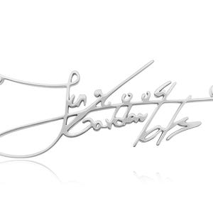 Close-up of a silver-colored chain necklace with a cursive signature pendant against a white background.