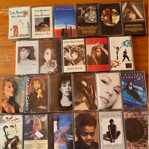 May include: A collection of vintage cassette tapes featuring various artists, including Kate Bush, Mariah Carey, Belinda Carlisle, Tracy Chapman, and Ed Brickell. The tapes are arranged in rows and are in various colors, including red, blue, green, and yellow.