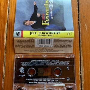 May include: A clear plastic cassette tape case with a black and white label. The label reads "Jeff Foxworthy/Greatest Bits" and includes a list of the songs on the tape. The Warner Bros. Records logo is in the upper left corner of the label. The tape is labeled with the number "1" and the text "24 74274 CR".
