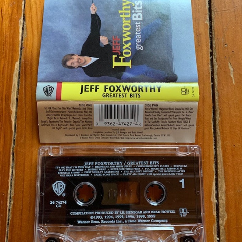 May include: A clear plastic cassette tape case with a black and white label. The label reads "Jeff Foxworthy/Greatest Bits" and includes a list of the songs on the tape. The Warner Bros. Records logo is in the upper left corner of the label. The tape is labeled with the number "1" and the text "24 74274 CR".
