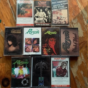 May include: A collection of vintage cassette tapes featuring rock and heavy metal bands. The tapes include albums by Ozzy Osbourne, Poison, Queensr&yuml;che, and Quiet Riot. The album art showcases various band logos and artwork.