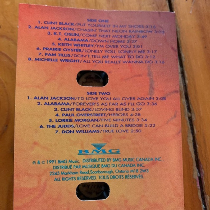 May include: A cassette tape case with a red, orange, and yellow background. The case lists the songs on the tape, including artists such as Clint Black, Alabama, and Alan Jackson. The case is labelled "Side One" and "Side Two". The BMG Music logo is at the bottom of the case.