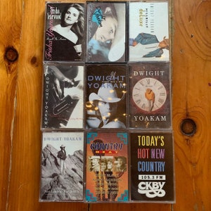 May include: A collection of nine cassette tapes, including artists Trisha Yearwood, Dwight Yoakam, and Hillbilly Deluxe. The tapes are arranged in three rows of three, with the titles and artist names visible on each tape.