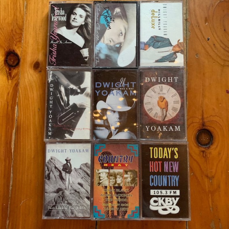 May include: A collection of nine cassette tapes, including artists Trisha Yearwood, Dwight Yoakam, and Hillbilly Deluxe. The tapes are arranged in three rows of three, with the titles and artist names visible on each tape.