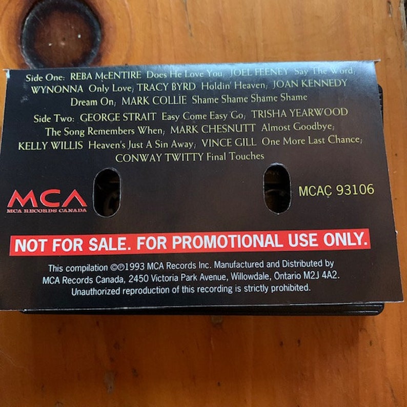 May include: A black cassette tape with a white label. The label has the text "MCA Records Canada" and "MCAC 93106". The label also lists the songs on the cassette tape, including artists such as Reba McEntire, Wynonna, George Strait, Trisha Yearwood, and more. The text "NOT FOR SALE. FOR PROMOTIONAL USE ONLY." is printed in white on a black background.